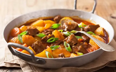 Un reconfortante estofado de ternera con patatas y zanahorias, adornado con cebolleta verde.
