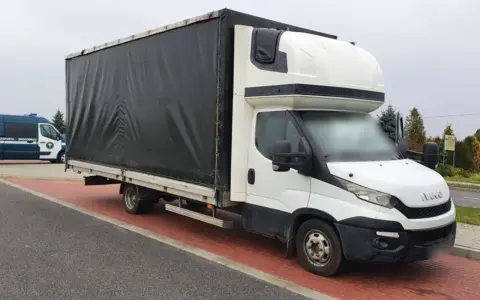 Biały bus Iveco z czarnym plandeką, ładowność 1,5 tony, stoi na czerwonej kostce brukowej.