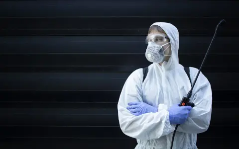 Persona con traje protector, mascarilla y gafas, sosteniendo un pulverizador. ¿Cuánto tiempo esperar después de fumigar?
