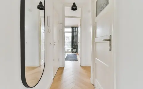 Un ampio specchio nel corridoio riflette le porte bianche e il pavimento in parquet.