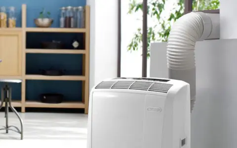 Climatiseur Rowenta portable, avec son tuyau d'évacuation dirigé vers une fenêtre. Un meuble de cuisine est visible à gauche.