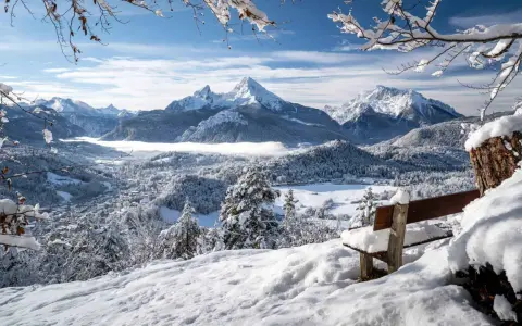 Ein verschneites Tal mit einem majestätischen Berg im Hintergrund. Eine Bank lädt zum Verweilen ein, perfekt für einen **ausflug im winter**.