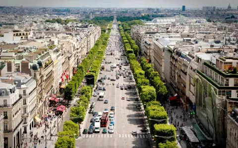 Vista aérea de la **Champs-Élysées** en París, con tráfico y peatones paseando entre los árboles y edificios.