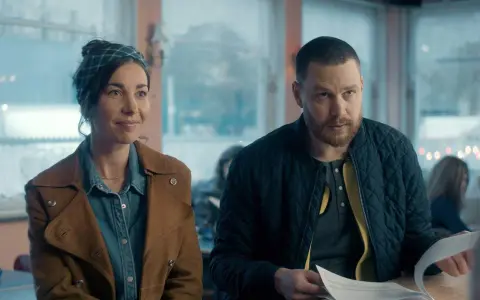En kvinna med scarf och en man med skägg sitter vid ett bord. De ser ut att vara med i en dansk serie på SVT.