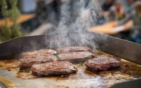 Mehrere saftige Rumpsteaks braten auf einer heißen Platte, Dampf steigt auf.
