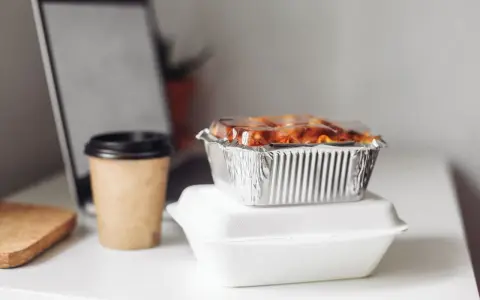 Gotowe jedzenie na wyjazd: zapiekanka w folii aluminiowej i kawa w kubku. Idealne na szybki lunch przy laptopie.