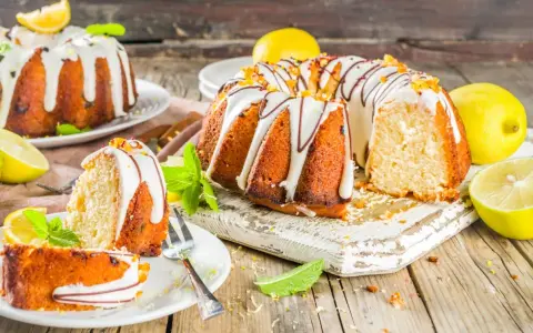 Najlepsza babka cytrynowa wilgotna na oleju, ozdobiona lukrem i skórką cytrynową, z kawałkami na talerzykach.