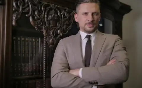 Mężczyzna w garniturze stoi przed regałem z książkami prawniczymi.