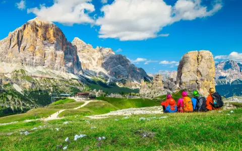 Quattro escursionisti ammirano un maestoso itinerario dolomiti, con cime imponenti e un rifugio alpino.