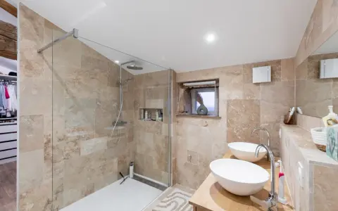 Salle de bain moderne avec douche à l'italienne, double vasque et carrelage en pierre naturelle. Un projet réussi pour refaire la salle de bain.
