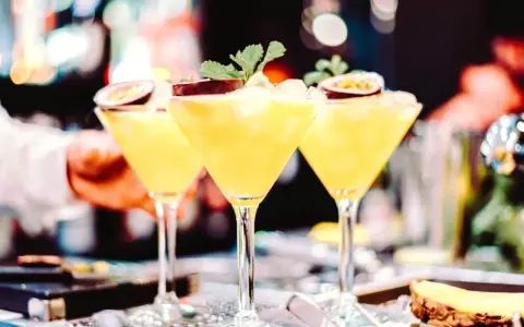 Trzy kieliszki z orzeźwiającą mango margarita, ozdobione połówkami marakui i listkami mięty, gotowe do podania.