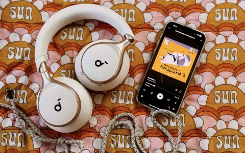 Białe słuchawki i smartfon z okładką audiobooka "Kocie kłopoty grzecznego psa" leżą na kolorowym tle z motywem słońc. Idealne do słuchania książek z lektorem.