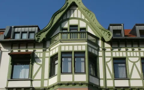 Elegancki ryzalit z wykuszem i zielonymi zdobieniami na fasadzie budynku, pod błękitnym niebem.