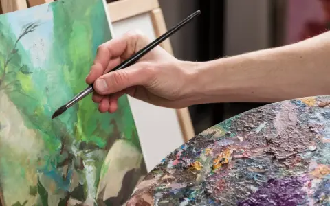 Main d'artiste appliquant la peinture sur une toile, palette colorée à proximité. Une belle technique de peinture en cours.