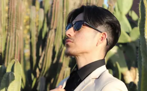 Uomo con abito beige e camicia nera, occhiali da sole, tra i cactus. Un look elegante per ogni occasione.
