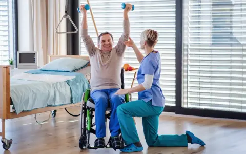 Starszy mężczyzna w wózku ćwiczy z hantlami pod okiem fizjoterapeutki. Czy rehabilitacje można odliczyć od podatku?