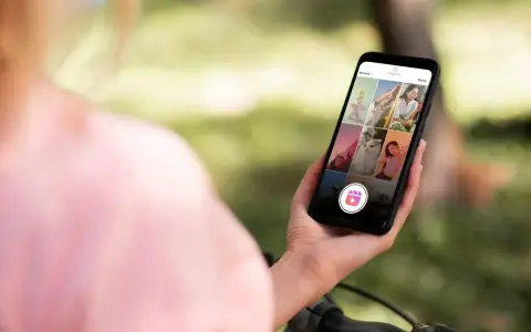 Osoba trzyma telefon z widokiem na ekran Instagrama, gdzie widać siatkę zdjęć i ikonę Reels. Dowiedz się, jak zrobić rolkę na Instagramie ze zdjęć.