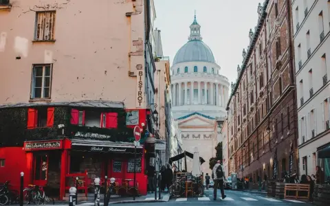 Urokliwa uliczka w paryskiej dzielnicy łacińskiej z czerwonym bistro i majestatycznym Panteonem w tle.
