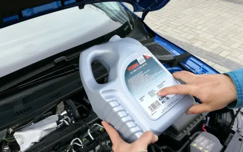 Osoba trzymająca kanister oleju silnikowego TITAN GT1 PRO C-3 SAE 5W-30 nad silnikiem. Czy można mieszać oleje silnikowe? Sprawdź specyfikacje!