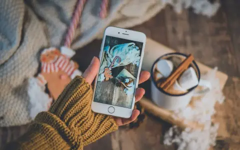 Hand holding a smartphone displaying a Christmas scene with gingerbread, candy cane, and marshmallows.