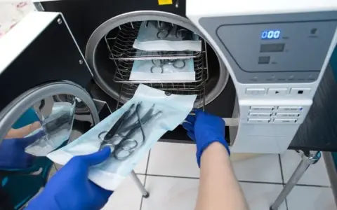 Handschuhe laden chirurgische Instrumente in einen Autoklaven zur Desinfektion und Sterilisation.