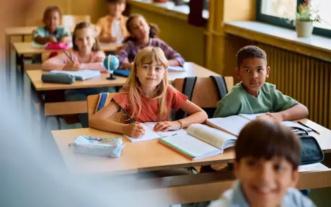 Dzieci w klasie skupione na lekcji. Uczennica pisze w zeszycie, obok niej leży piórnik. To pokazuje, co na koncentrację u dzieci: nauka i zaangażowanie.