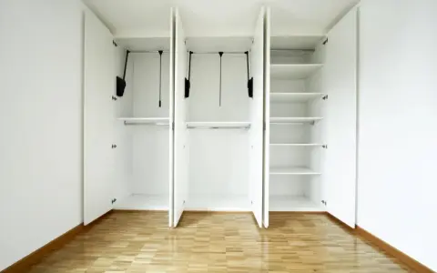 Interno di un armadio bianco a tre ante, vuoto, con ripiani e barre appendiabiti. Un esempio di come costruire un armadio funzionale.