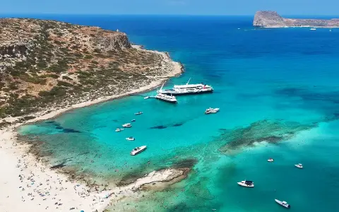 Rajska plaża z turkusową wodą, statkami i ludźmi. Kreta wschodnia atrakcje zachwycają!