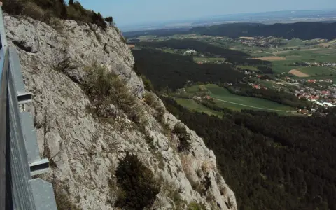Widok z **Hohe Wand** na dolinę z lasami i wioskami. Stroma, skalista ściana po lewej stronie.