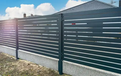 Nowoczesne ogrodzenie z poziomych paneli, osadzone na betonowym cokole. To świetne rozwiązanie co zamiast podmurówki pod ogrodzenie, zapewniające estetykę i trwałość.