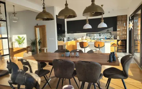 Oświetlenie salonu inspiracje: industrialne lampy wiszące nad drewnianym stołem, nowoczesna kuchnia w tle.