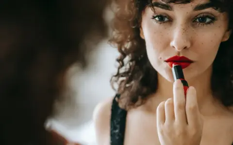 Donna con capelli ricci applica un trucco con rossetto rosso vibrante, creando un look audace e seducente.