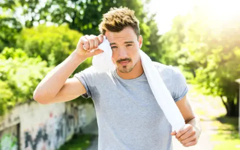 Ein Mann wischt sich mit einem Handtuch den Schweiß von der Stirn. Er hat gerade Sport getrieben und schwitzen Sportler mehr, wenn es warm ist.