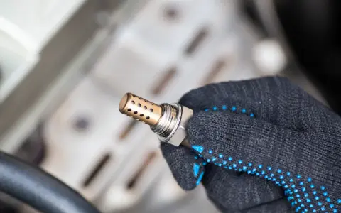 Defekte Lambdasonde als Ursache für die Motorkontrollleuchte. Ein Mechaniker hält das Bauteil in der Hand.