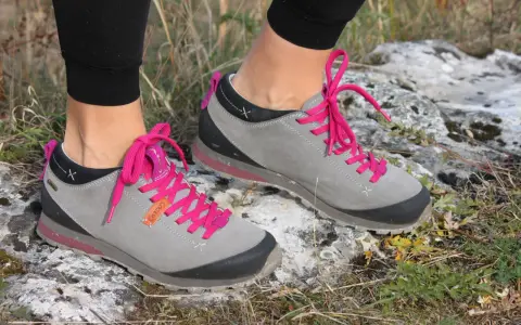 Szare buty trekkingowe Aku Bellamont z jaskrawymi, różowymi sznurówkami na kamienistym, trawiastym podłożu.