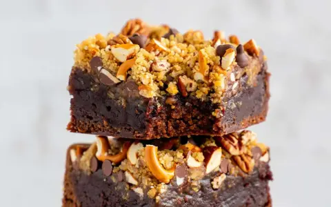 Zwei gestapelte, saftige fudge brownies, garniert mit Brezelstückchen, Nüssen und Schokostückchen.