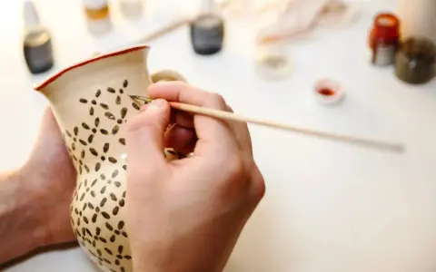 En person målar keramik hemma, dekorerar en mugg med små mönster.