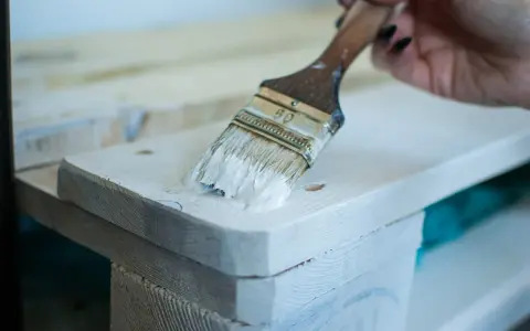 Application de peinture glycéro sur bois brut, sans poncer. La brosse dépose une couche blanche sur la surface.