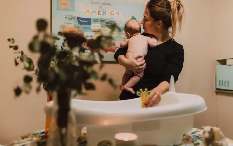 Mamma håller sitt barn redo för bad. Frågan "hur ofta bada bebis" dyker upp när man förbereder badkaret med leksaker.