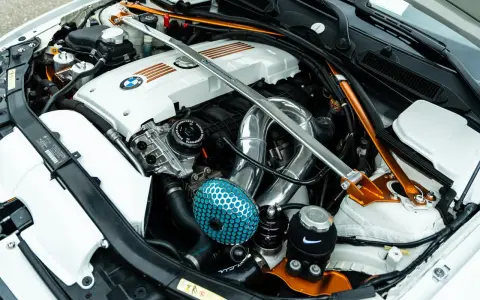 Custom BMW engine bay with a silver strut bar and orange accents. If your engine is ticking, check the oil level and listen for unusual noises.