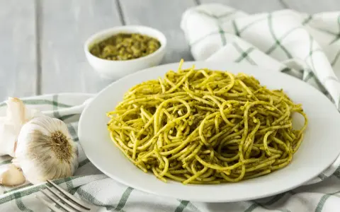 Pyszny makaron z pesto, podany na białym talerzu, obok czosnku i miseczki z sosem.
