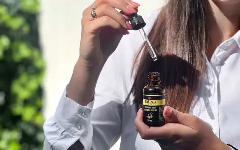 Kobieta trzyma buteleczkę z olejkiem Sattva i pipetkę z serum do włosów.