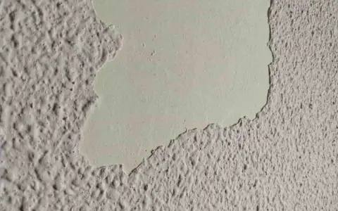 Detalle de pared con gotelé descascarillado, mostrando la capa inferior lisa. Ideal para aprender como quitar gotele.