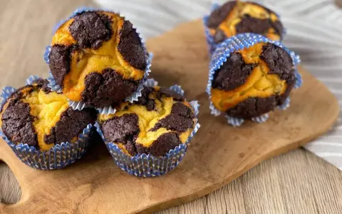 Schokoladen-Vanille-Zupfkuchen-Muffins in blauen Papierförmchen auf einem Holzbrett.