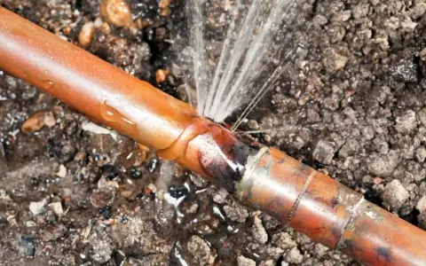 Une fuite sur un tuyau de cuivre, l'eau jaillit d'une fissure dans le sol.