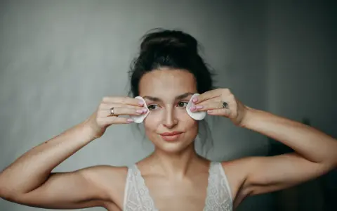 Kobieta wykonuje demakijaż oczu wacikami. Delikatne mycie twarzy olejem to jej rytuał.