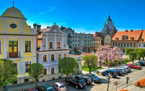 Kolorowy rynek w Kluczborku z zabytkowymi kamieniczkami, kwitnącą magnolią i wieżą kościelną. Kluczbork atrakcje zachwycają.