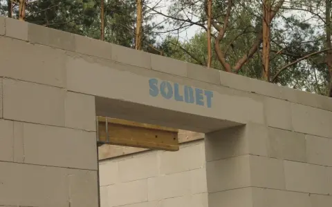 Ściana z bloczków betonowych z widocznym nadprożem marki SOLBET. Widać, jak nadproże ile powinno zachodzić, by zapewnić stabilność konstrukcji.