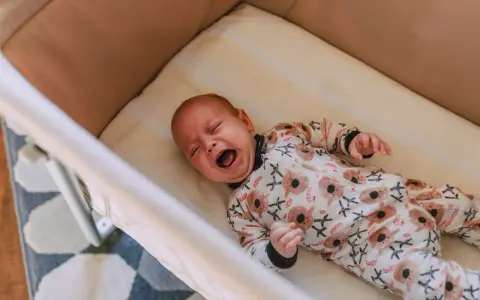 Bebé llorando en su cuna, con un pijama de koalas. Un momento difícil para dejar llorar a un niño de 2 años para dormir.