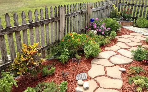 Natürliche Steinplatten formen einen geschwungenen Gartenweg, umgeben von bunten Blumen und grünen Pflanzen. Tolle Gartenweg Ideen für ein idyllisches Zuhause.
